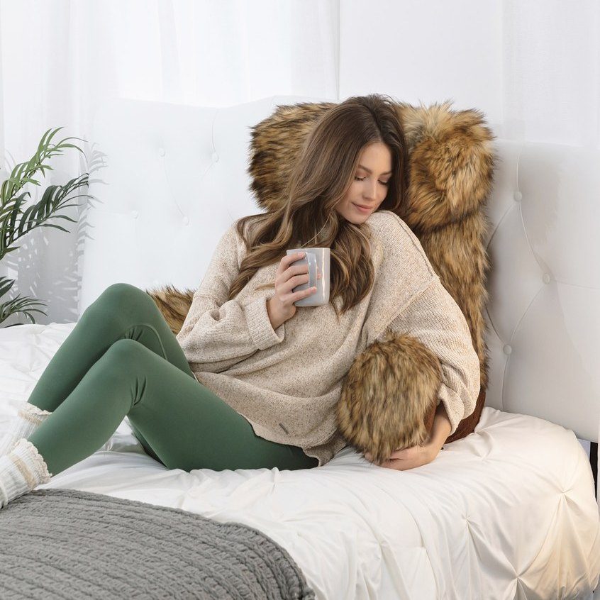 Woman with a mug relaxing on a faux-fur pillow